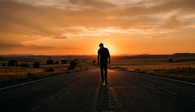 Person walking forward on empty highway at sunset — moving on and starting a new journey